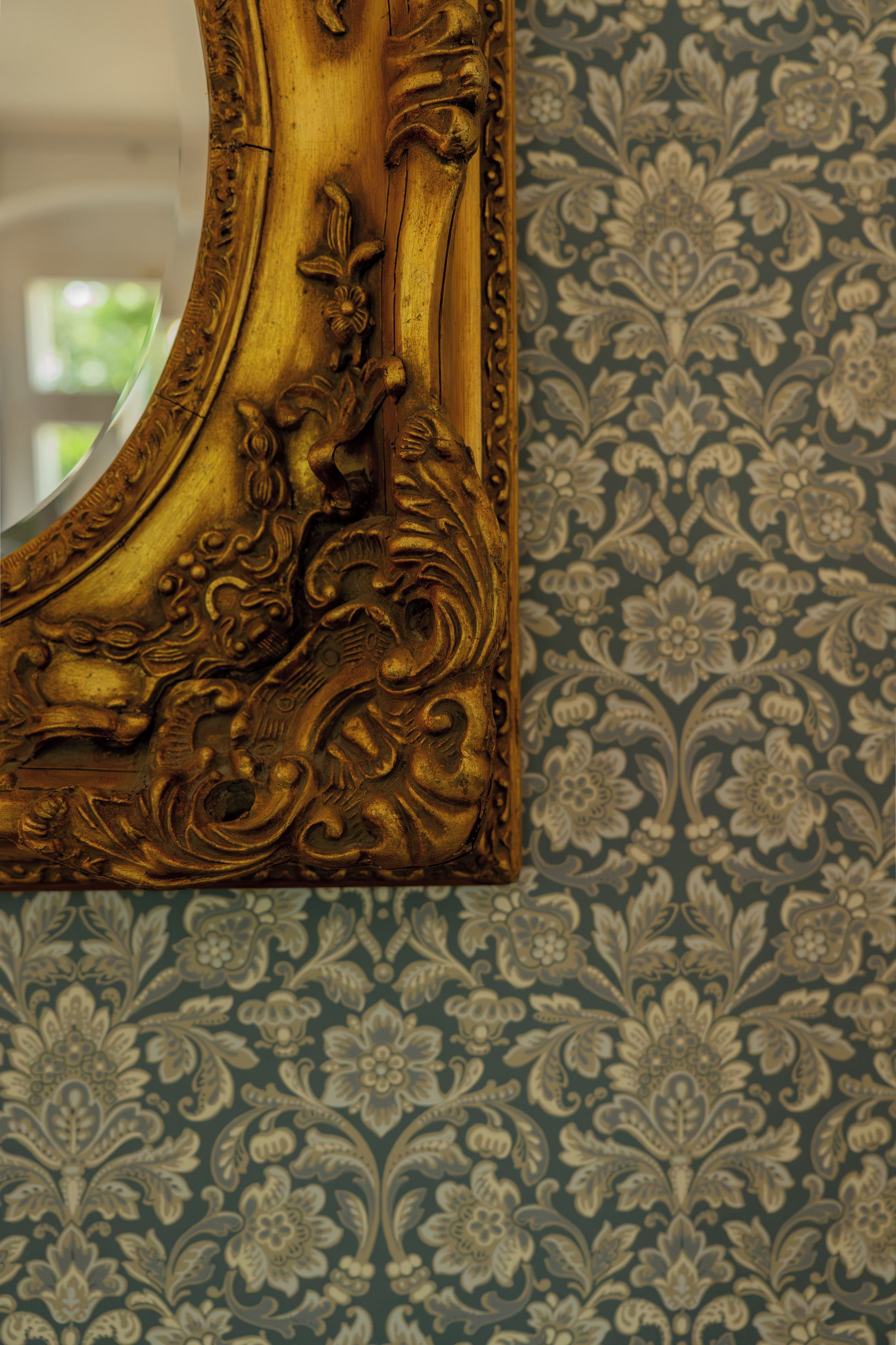 A wall with ornate, gold-colored woodwork and a patterned wallpaper.