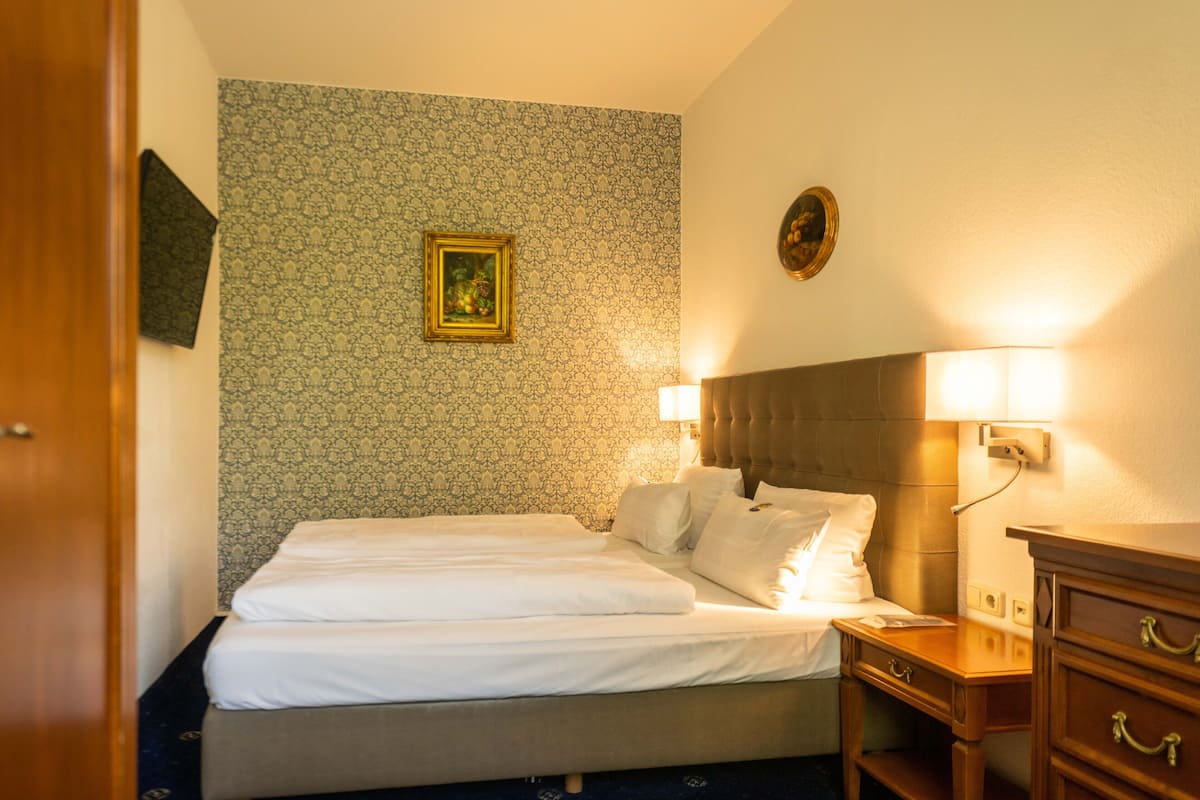 A hotel room with a neatly made bed, a bedside table with a lamp, and a dresser.