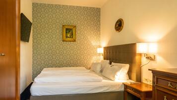 A hotel room with a neatly made bed, a bedside table with a lamp, and a dresser.