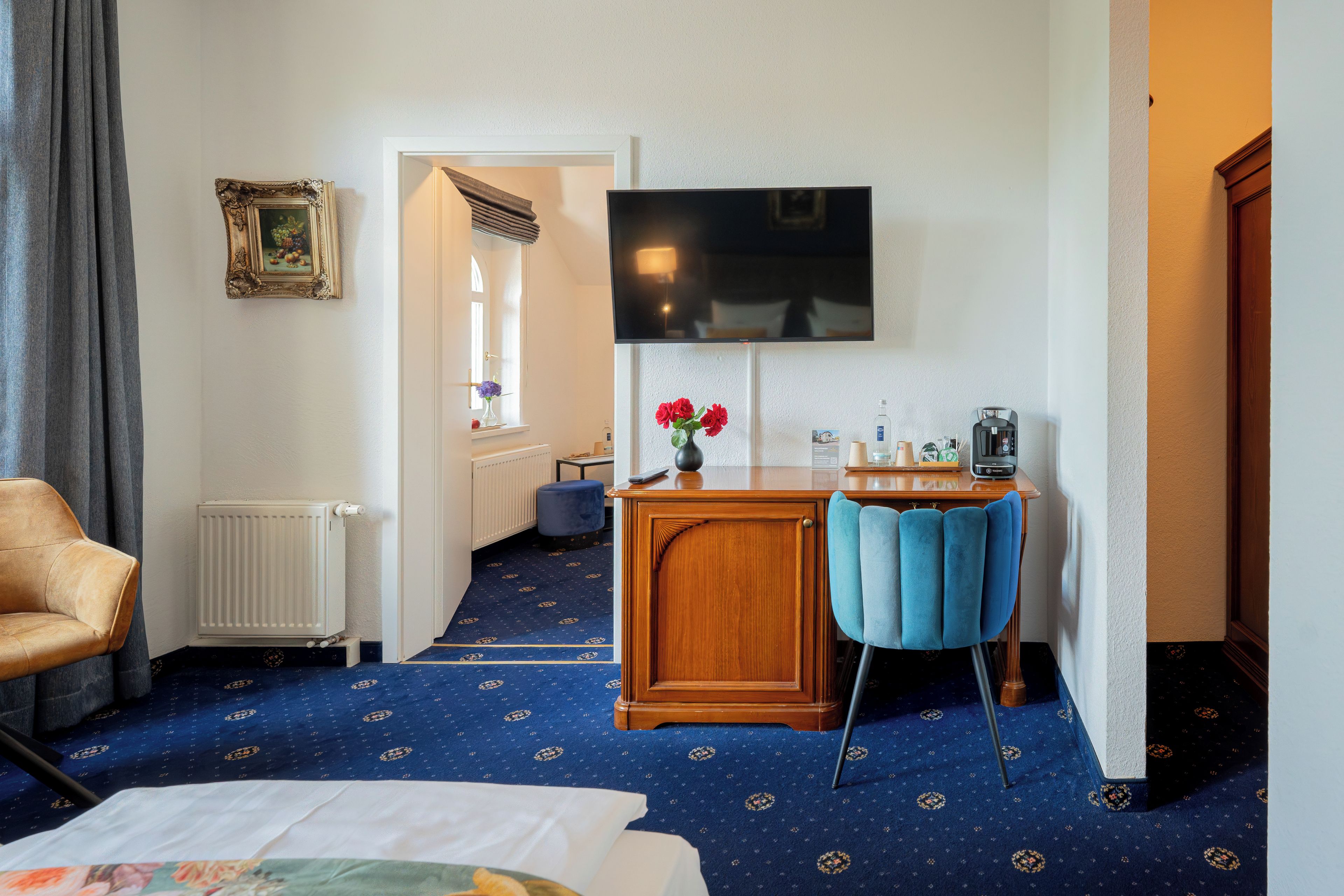 A hotel room with a bed, a desk with a chair, a television, and a window with curtains.