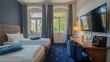 Habitación de hotel con dos camas, un escritorio con cafetera, televisor y vista a zonas verdes.