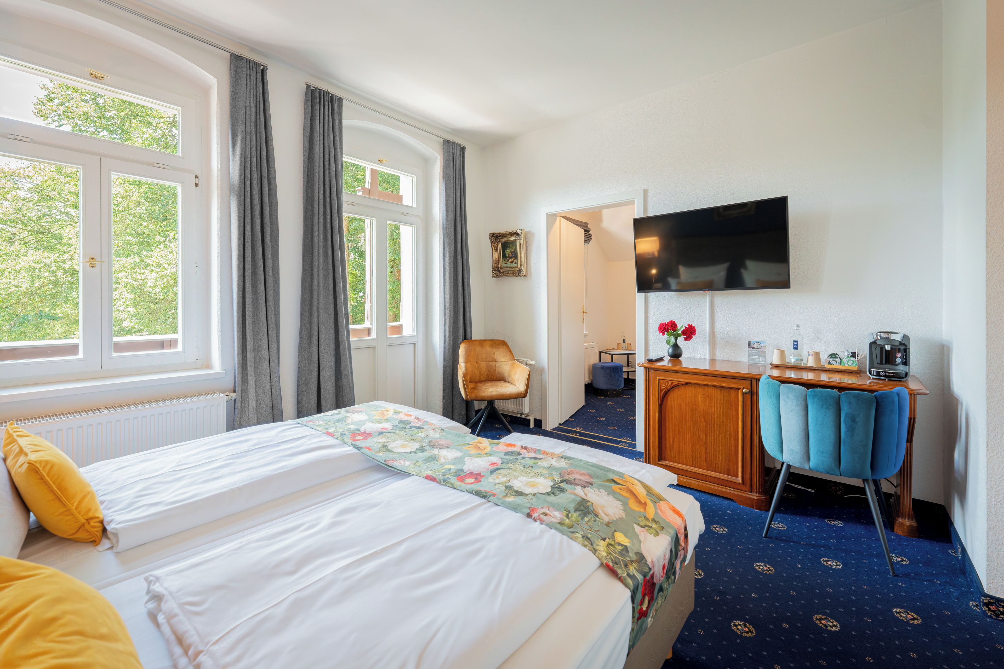 Ett hotellrum med en säng, ett skrivbord, en stol, en tv och utsikt över grönområden utanför.