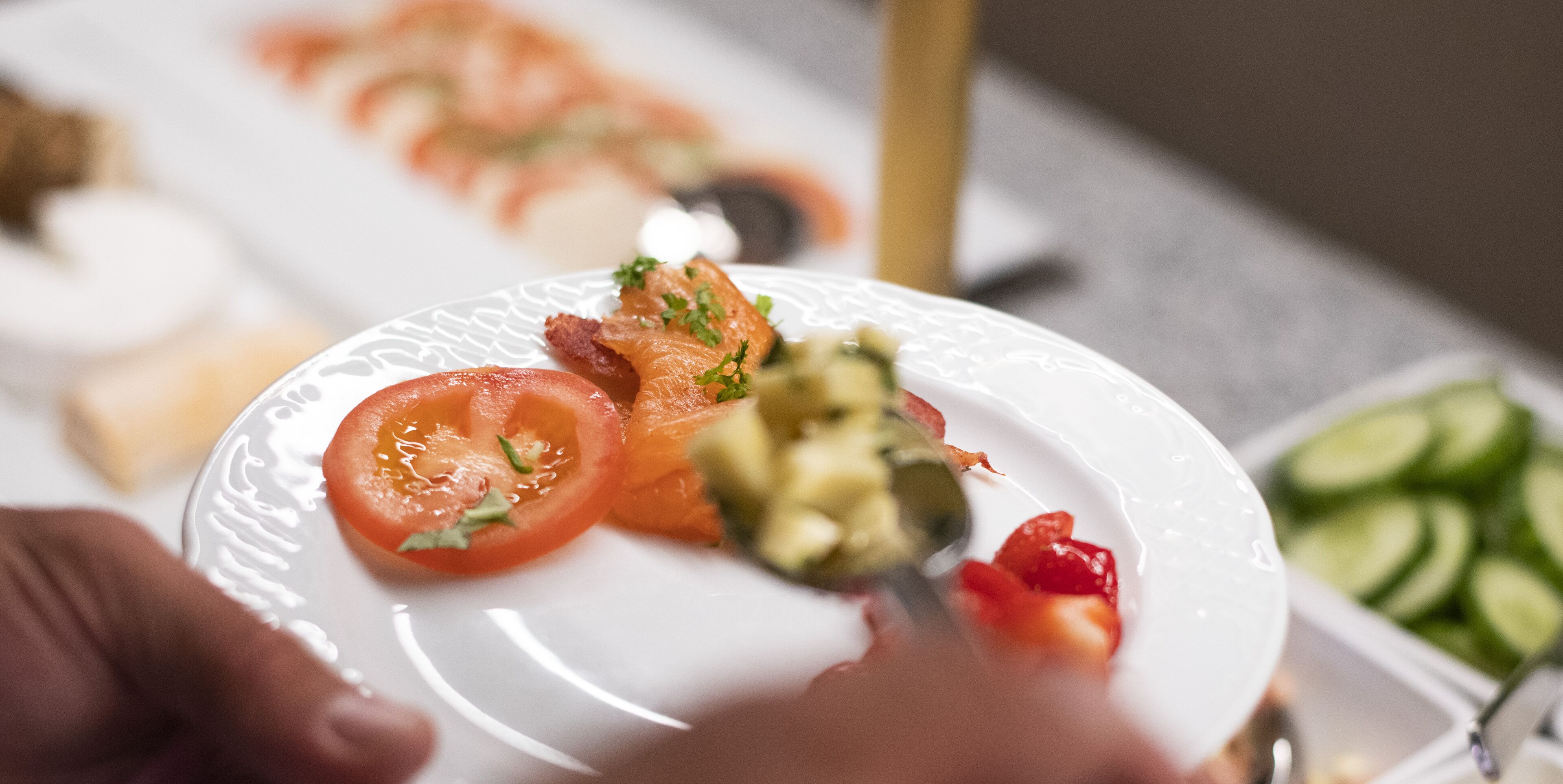 A plate with sliced tomatoes, avocado, and bacon, with a hand holding a fork.