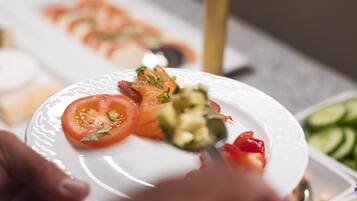 A plate with sliced tomatoes, avocado, and bacon, with a hand holding a fork.
