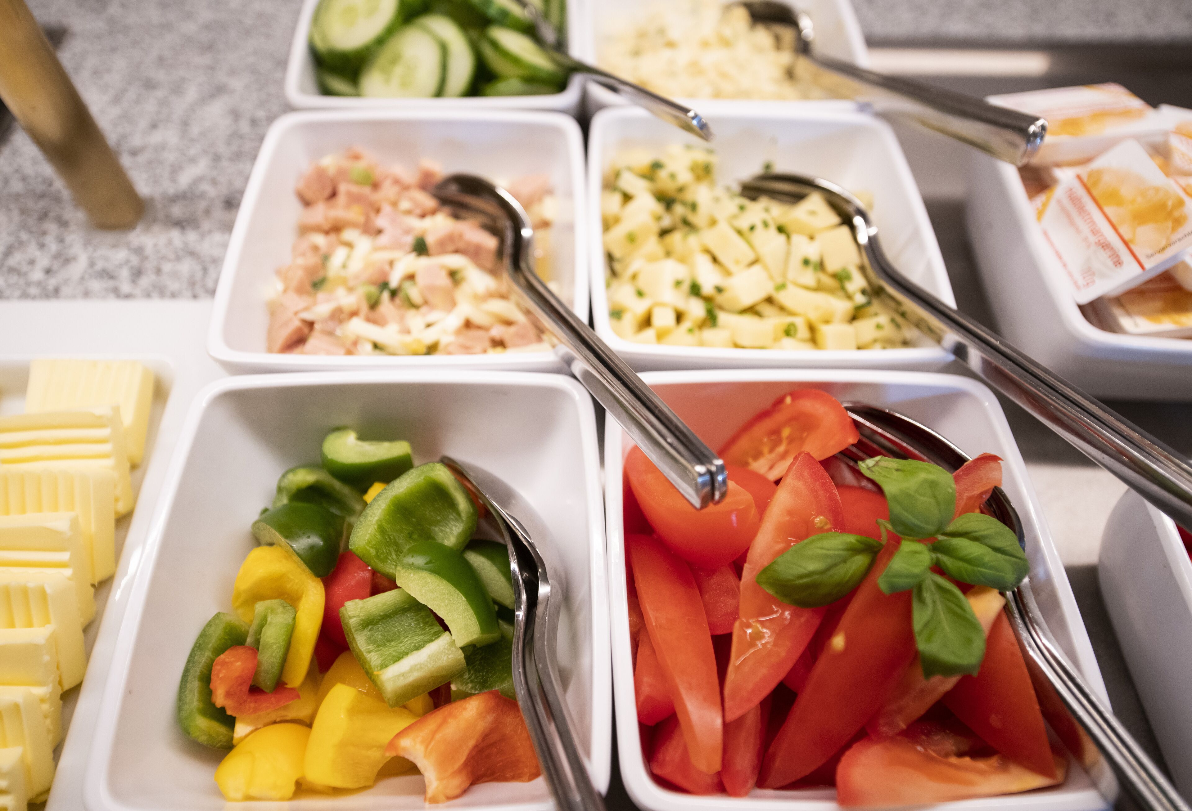 Un bufé con diversas opciones de comida, incluyendo verduras, queso y carnes.
