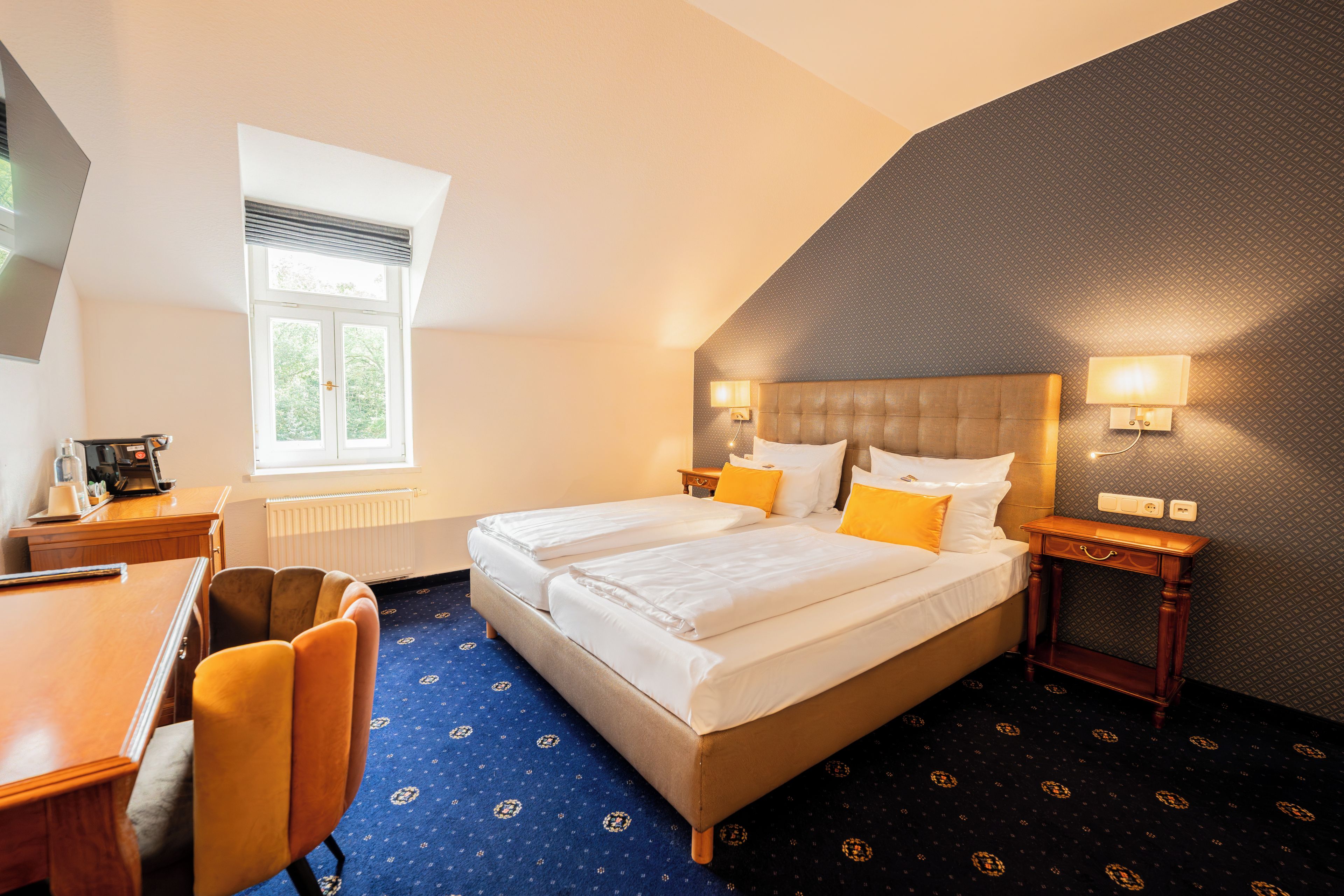 Une chambre d’hôtel avec un lit double, un bureau, une chaise, une fenêtre et un tapis à motifs.