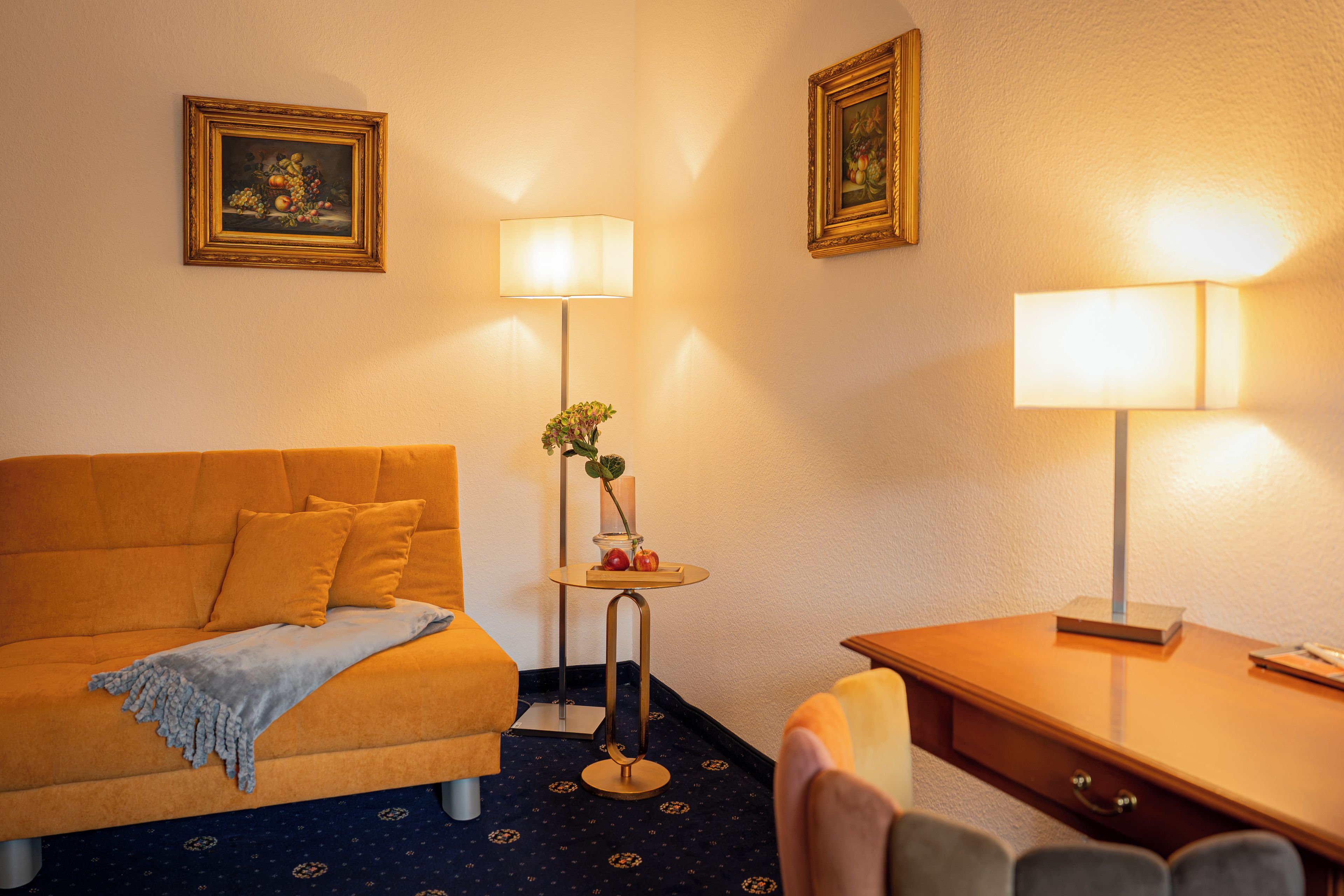 Et hotelværelse med en seng, et skrivebord, to lamper og billeder på væggene.