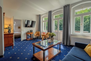 A hotel room with a large window, a flat-screen TV, a sofa, a coffee table, and a bed. - Historische Spitzgrundmühle Coswig (Coswig)