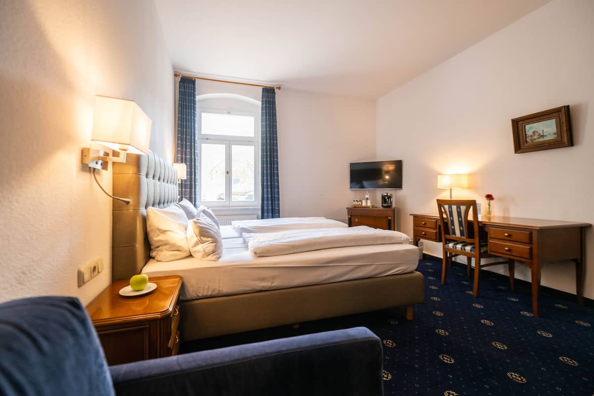 A hotel room with a bed, a desk, a chair, a television, and a window with curtains.