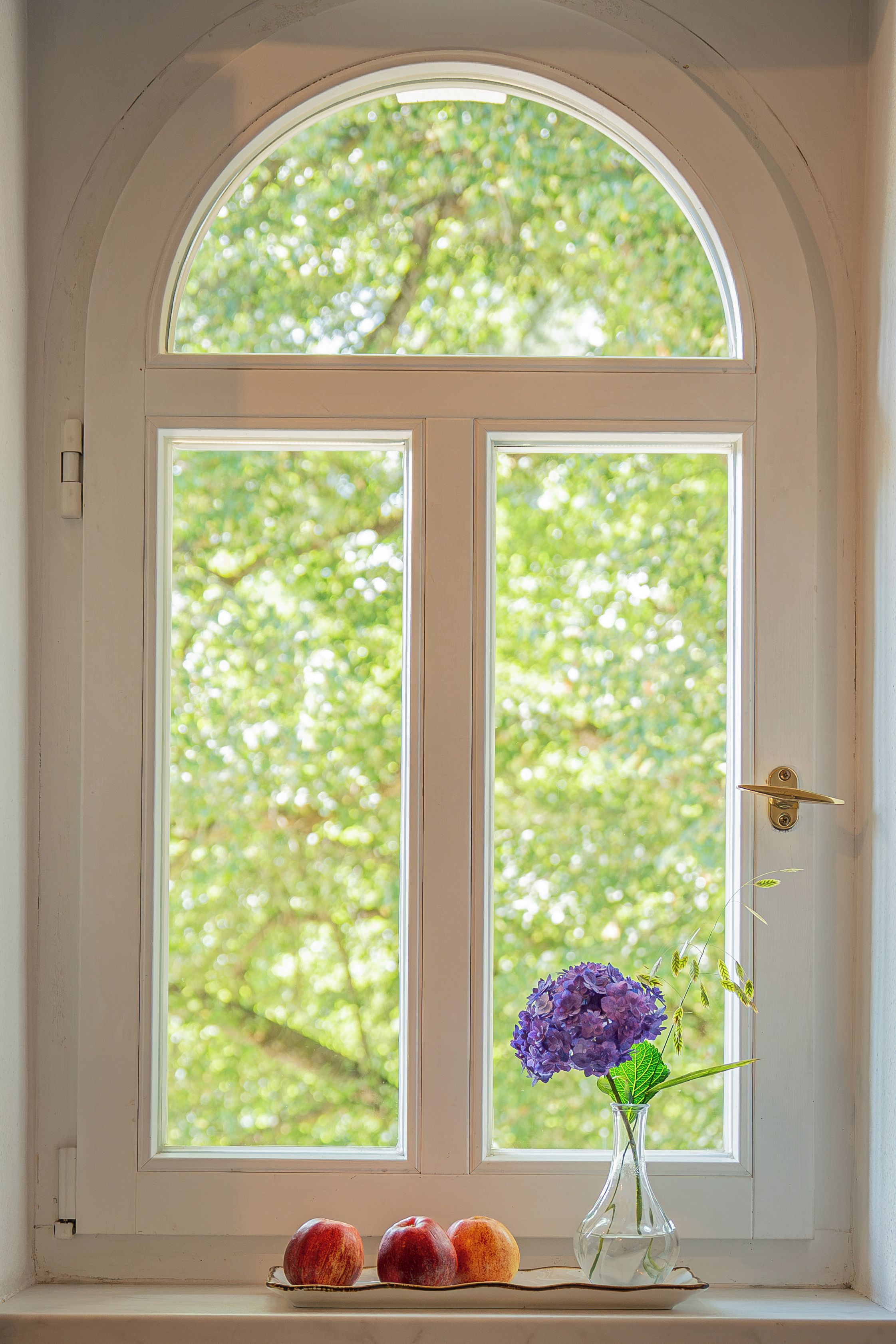 Eine weiße Tür mit einem halbkreisförmigen Fenster darüber, einem Messing-Türgriff und einem kleinen Tisch mit einer Vase voller lila Blumen und zwei Äpfeln.