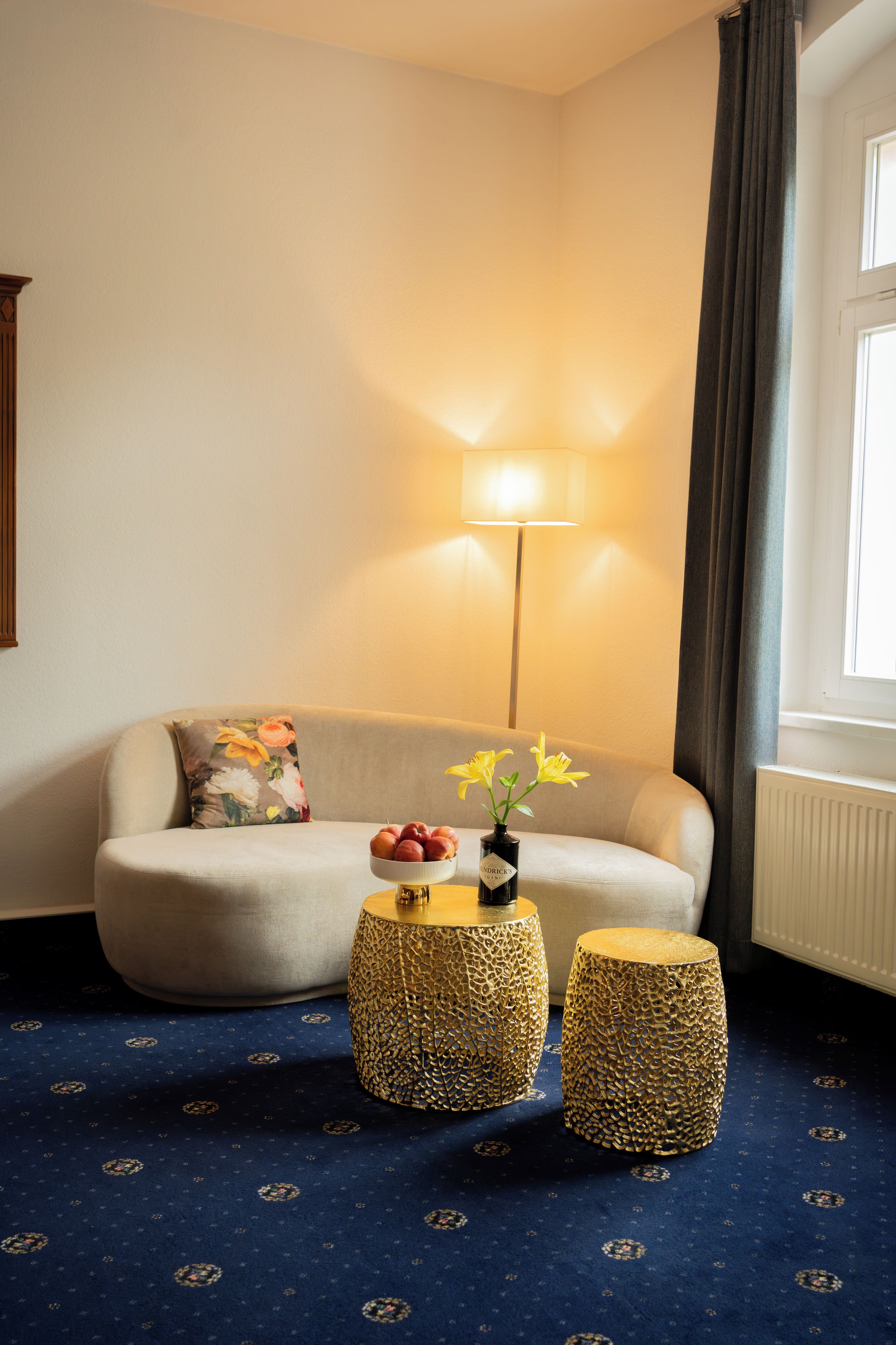 Een kamer met een bank, twee ronde bijzettafels, een lamp en een raam met gordijnen.