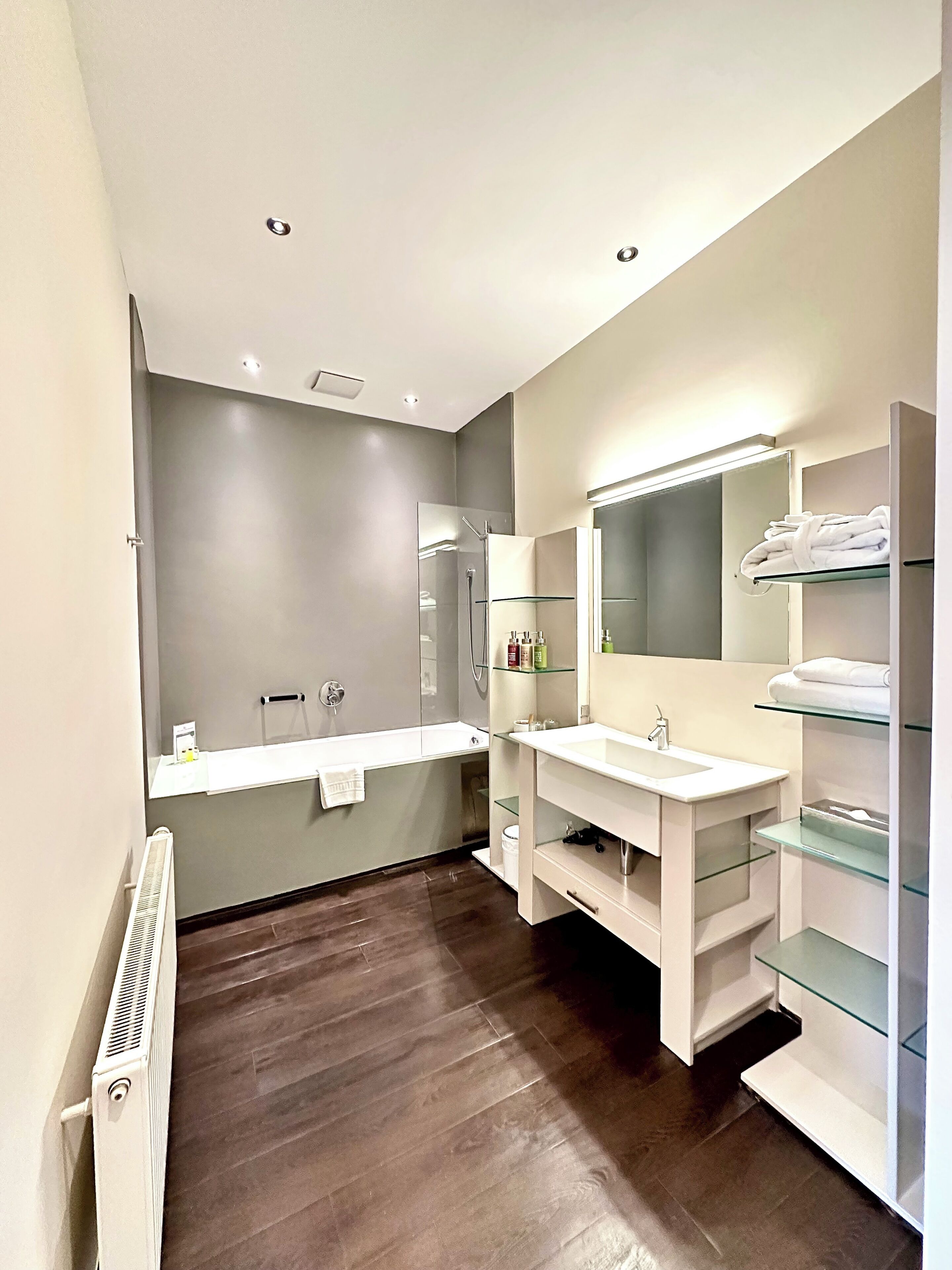 A modern bathroom with a glass shower enclosure, a white vanity with a mirror, and a built-in radiator.