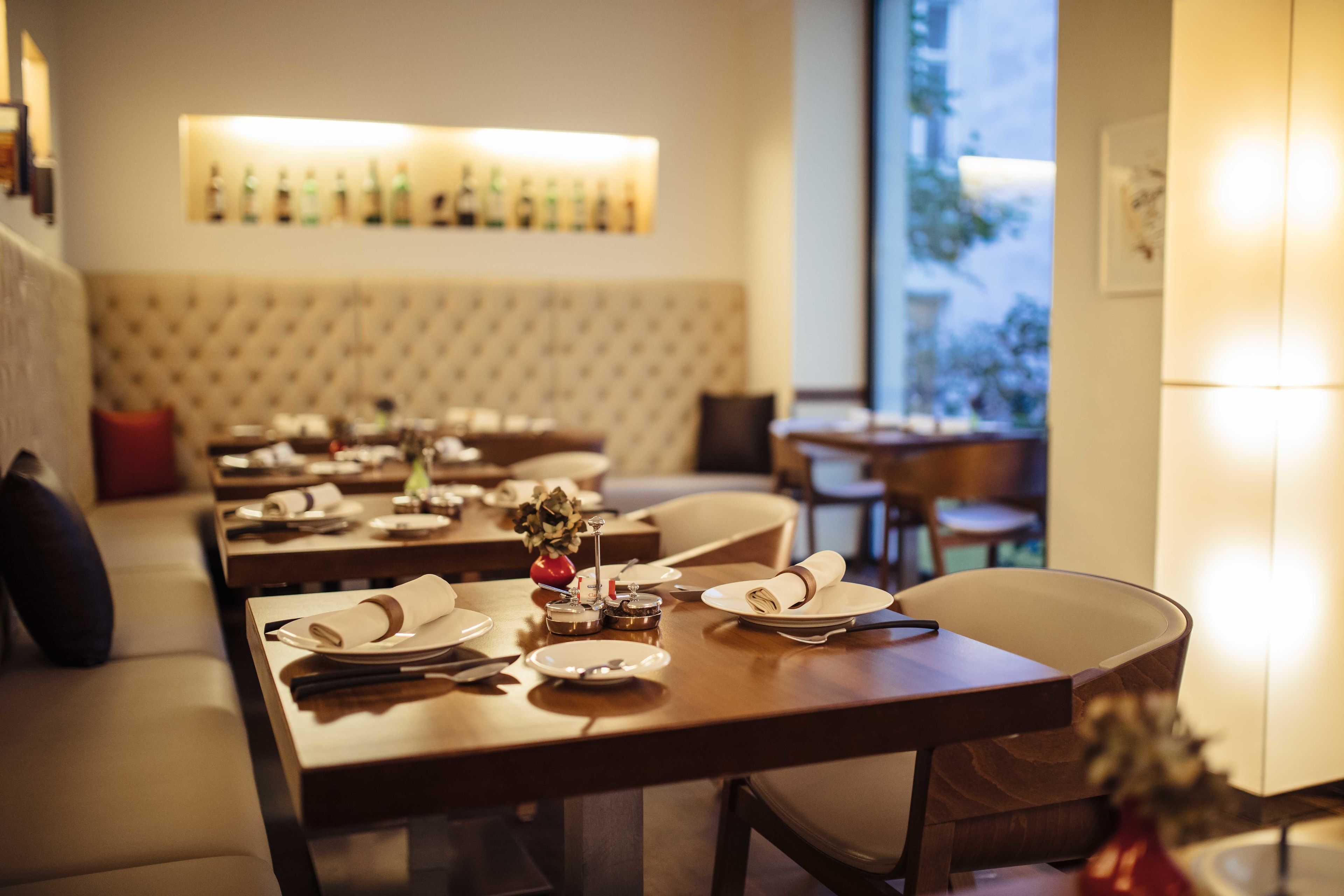 A dining area with tables set for two, a tufted headboard, and a wall-mounted liquor display.