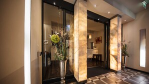 A hotel lobby with a checkered floor, marble pillars, and potted plants. - Hotel Rathaus Wein & Design (Vienna)
