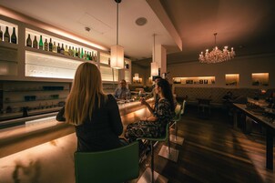 Een bar met een lange toonbank, flessenkasten en een kroonluchter.