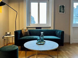 Un soggiorno con un divano verde, un tavolino con una caraffa di vetro, una lampada e un telefono su un comodino.
