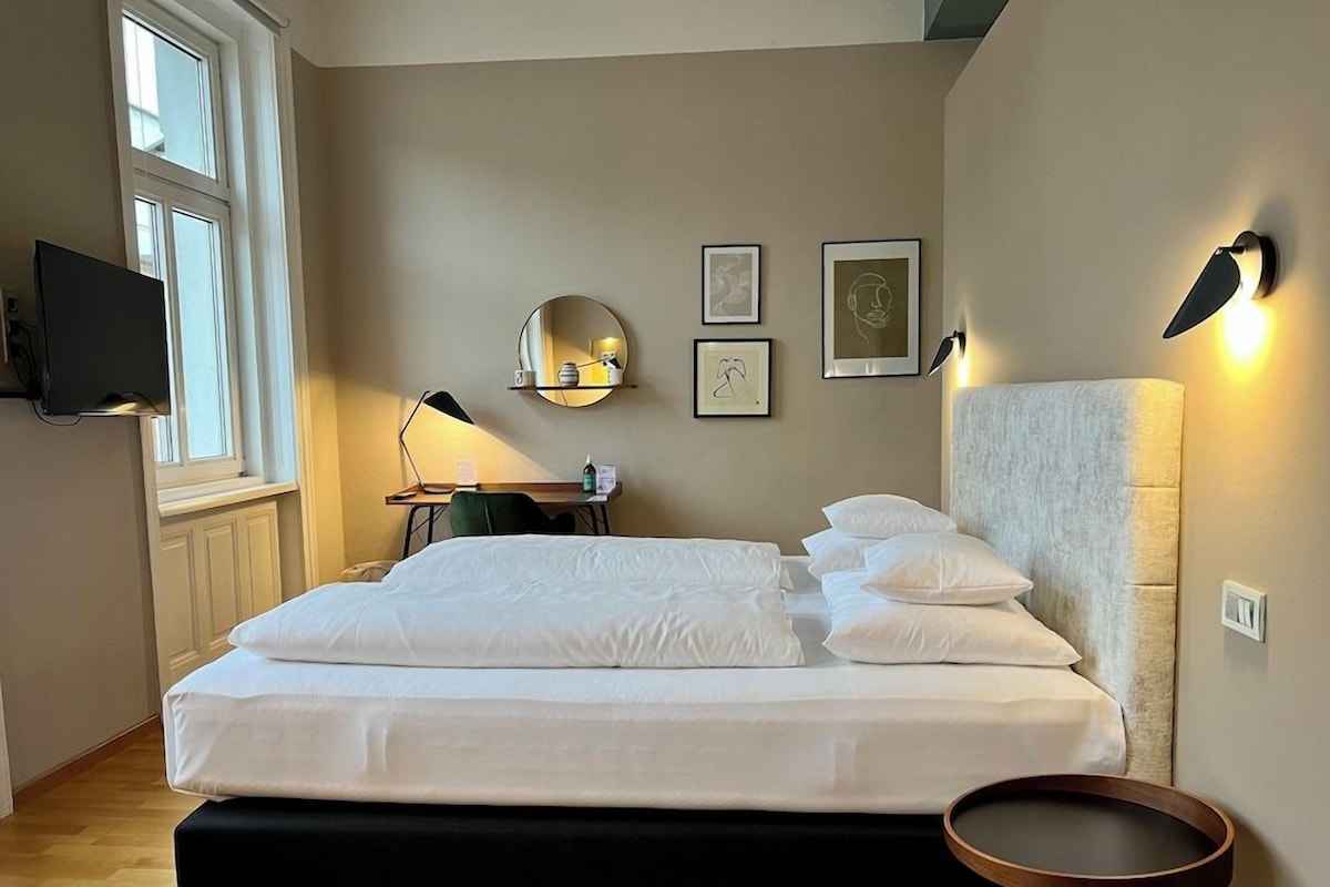 Habitación de hotel con cama, mesita de noche, lámpara, decoración en la pared y televisor montado.
