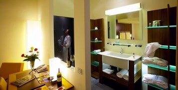 Casa de banho de hotel com lavatório, espelho e prateleiras para toalhas.