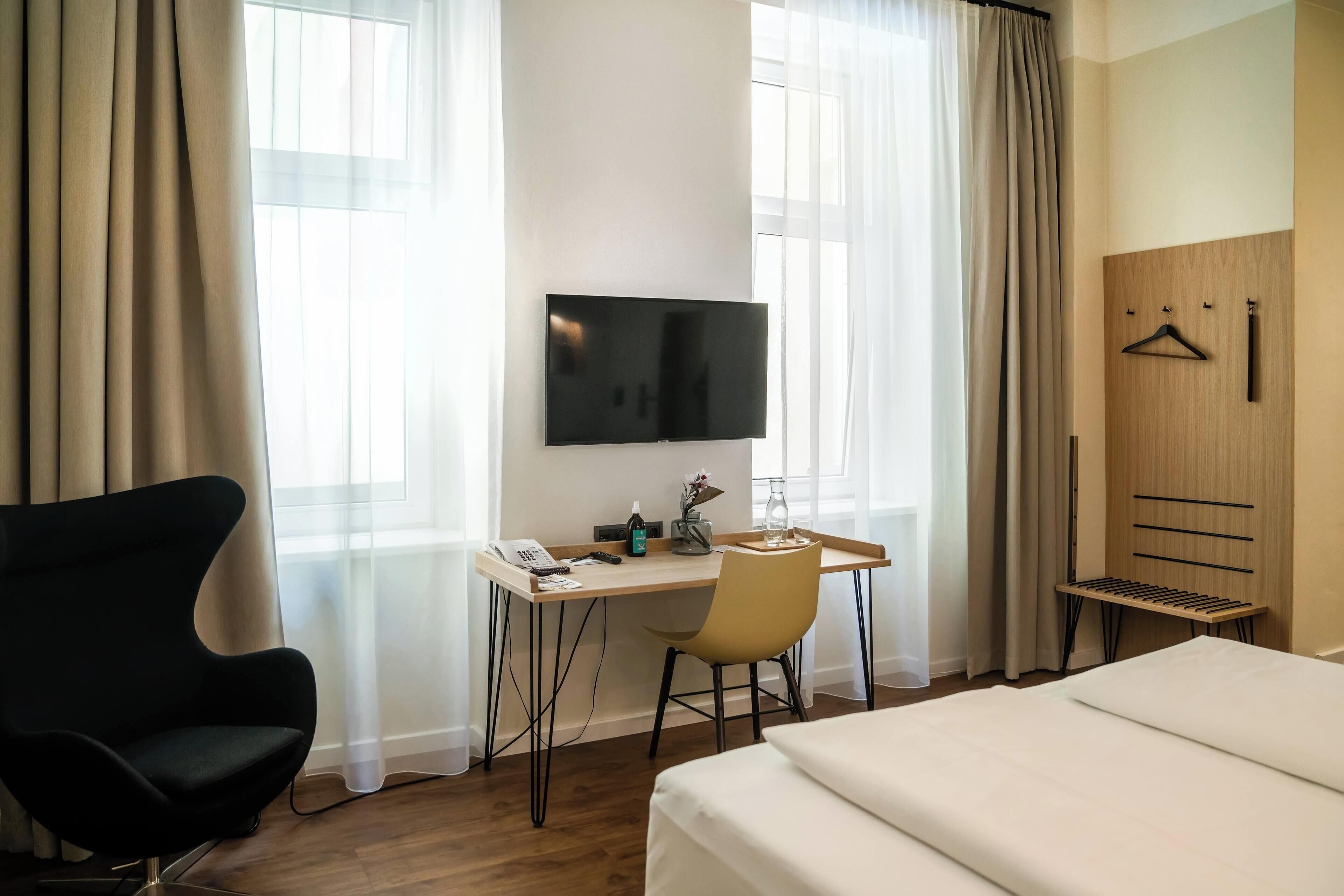 Una habitación de hotel con cama, escritorio con silla, televisión y armario.