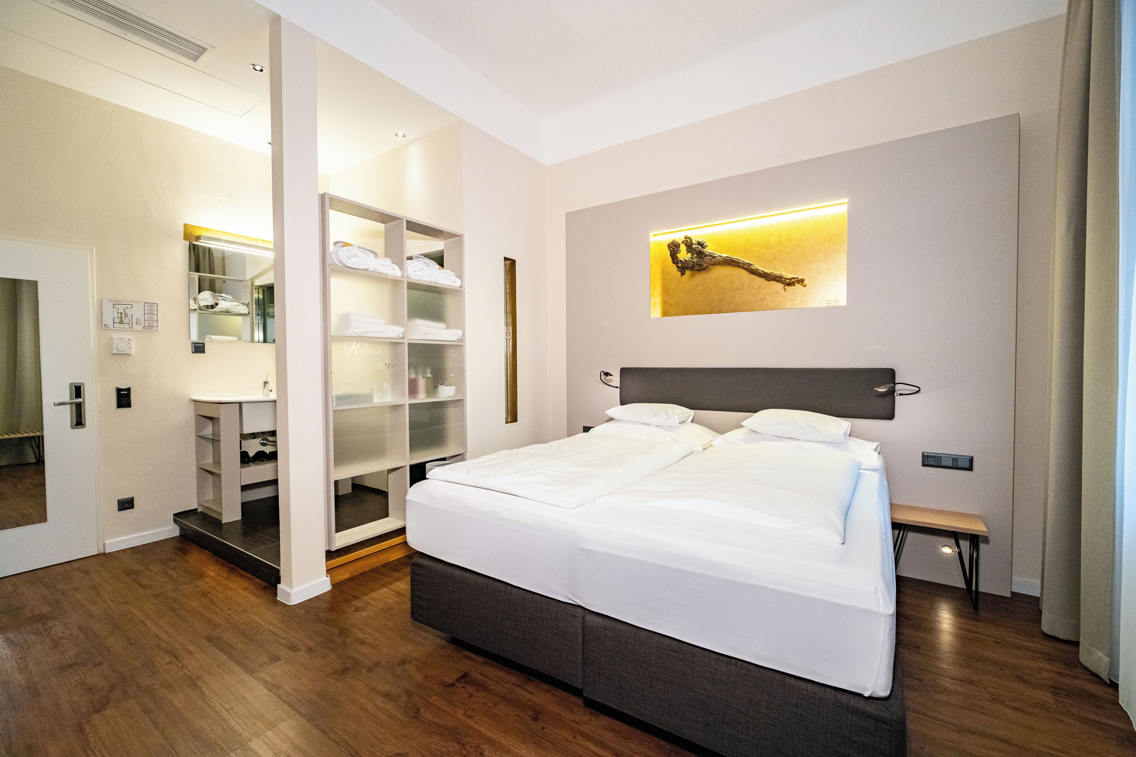 Una habitación de hotel moderna con una cama grande, armario empotrado, mesita de noche y una obra de arte colgada en la pared.