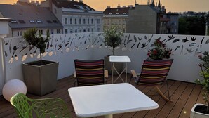 A rooftop terrace with a white table and two striped chairs, surrounded by potted plants and a decorative fence. - Hotel Rathaus Wein & Design (Vienna)