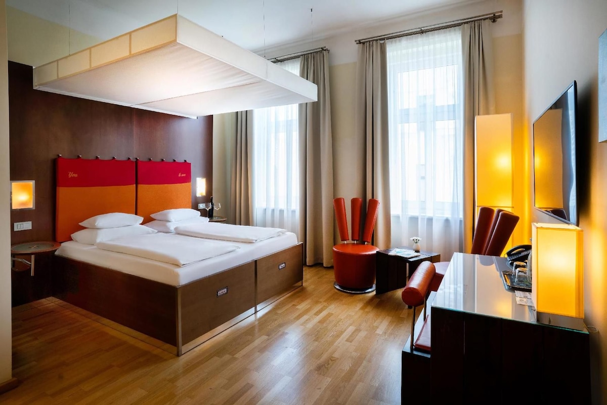 Habitación de hotel con una cama grande, un escritorio, una silla, un televisor y una ventana con cortinas.
