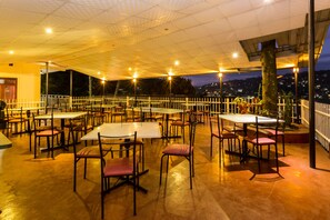 An outdoor dining area with tables and chairs, a covered roof, and a view of the city at night. - Tamarind Tree Inn (Kandy)