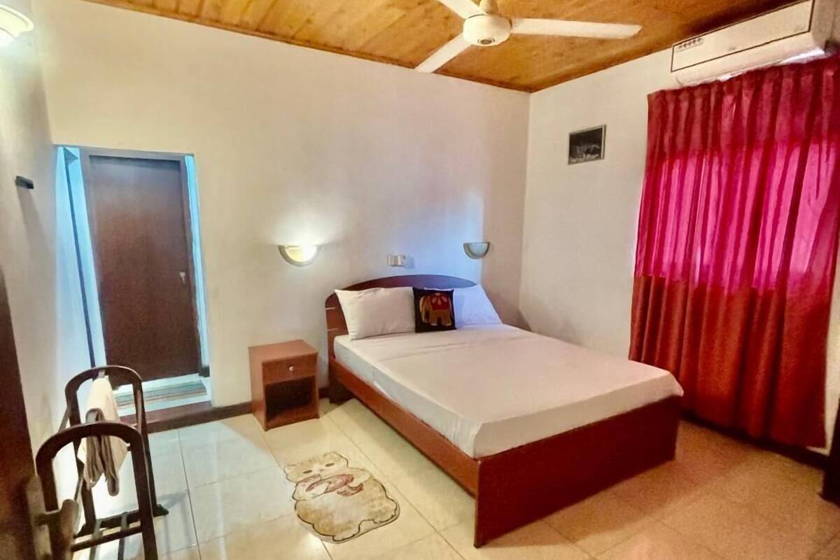 A bedroom with a bed, a ceiling fan, a window, a door, and a red curtain.