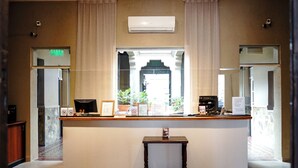 Zona de recepción con mostrador, certificados enmarcados, una pequeña mesa y vista al exterior a través de una ventana.