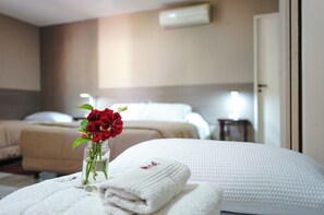 A hotel room with two beds, a white textured bedspread, a vase with red flowers, and a folded white towel on a bedside table. - Hotel de la Linda (Salta)