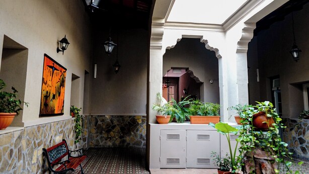 Un patio con muros de piedra, plantas en macetas, un banco y una obra de arte enmarcada.