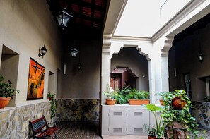 A courtyard with stone walls, potted plants, a bench, and a framed artwork. - Hotel de la Linda (Salta)
