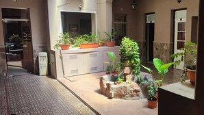 Un patio con plantas en macetas, un banco de piedra y una puerta que da a una habitación.