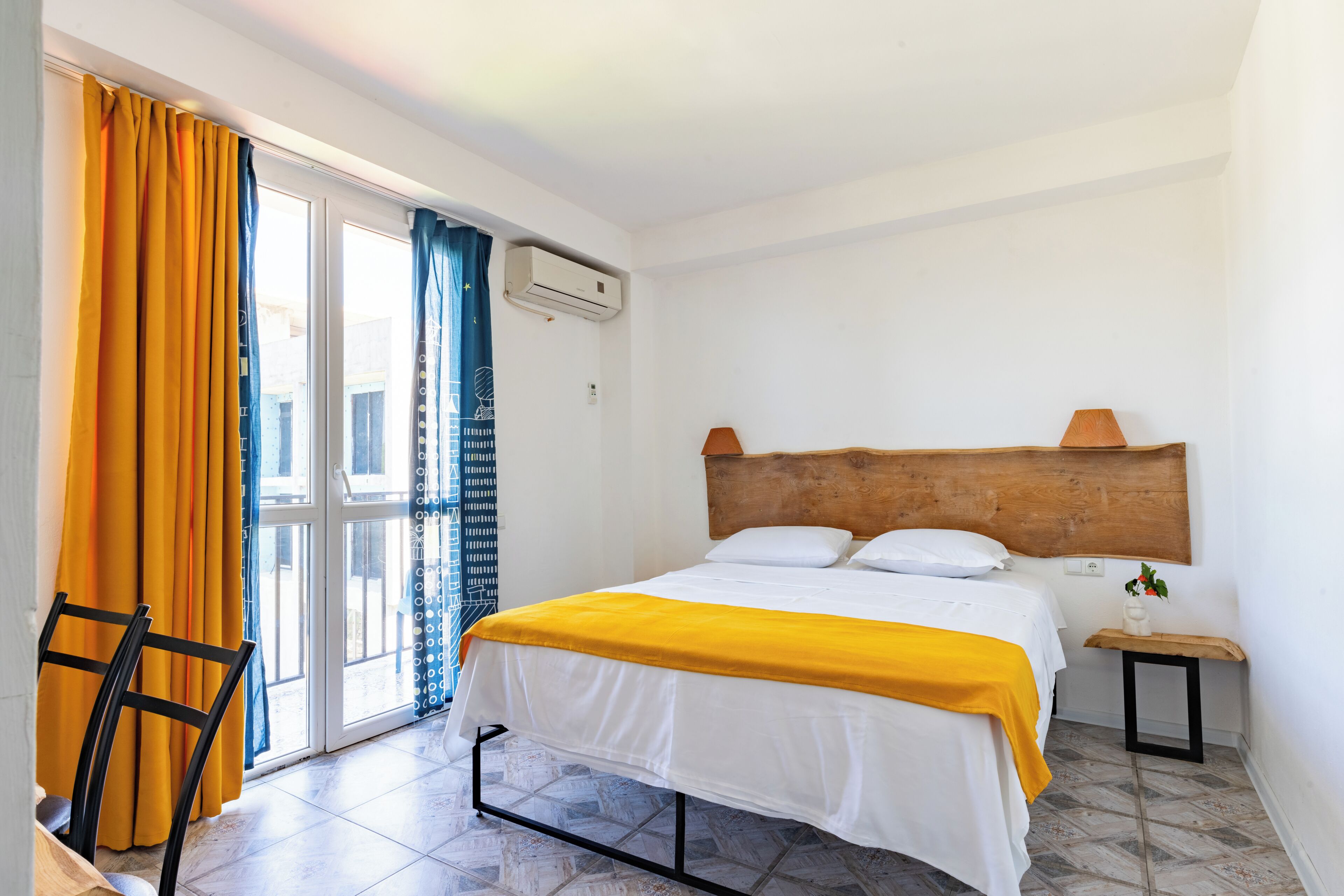A bedroom with a bed, a wooden headboard, a nightstand, a chair, and a window with curtains.