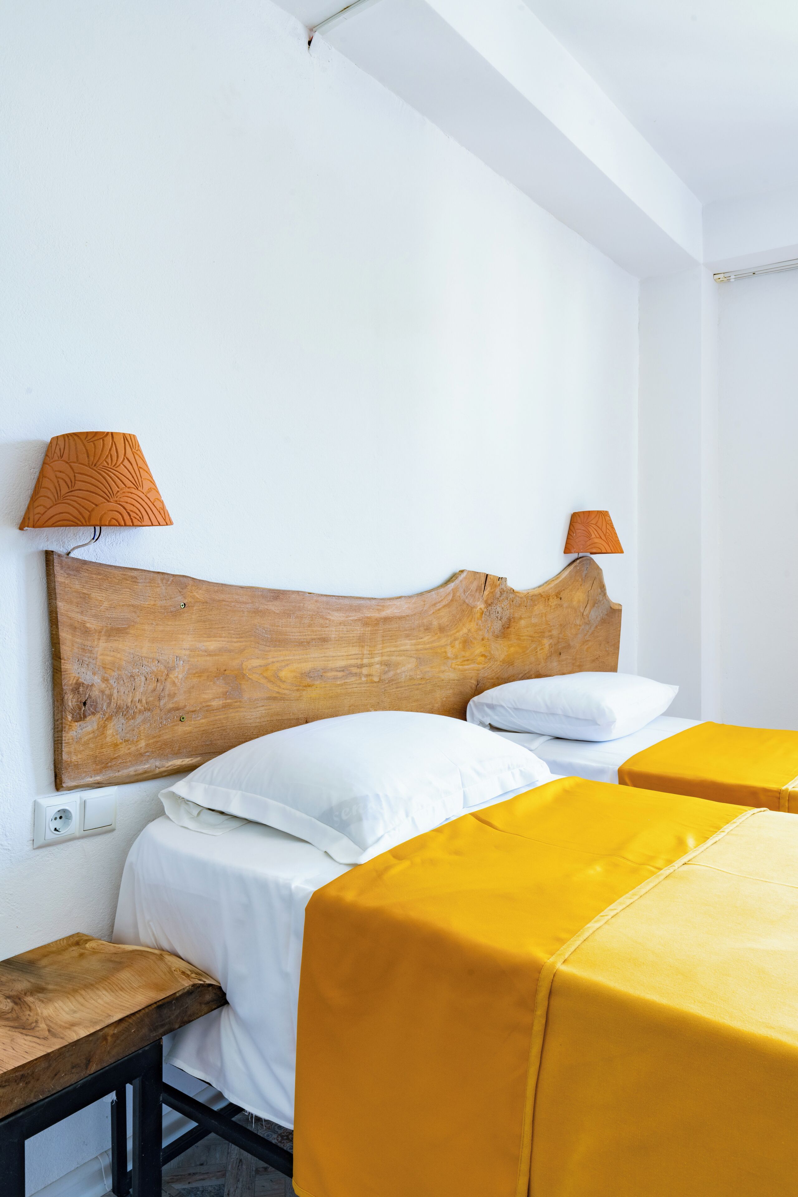 A hotel room with a wooden headboard, two beds with white bedding, and two lamps with orange shades.