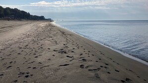 Ein Strand mit Fußspuren, einem klaren Himmel und einer entfernten Brücke.