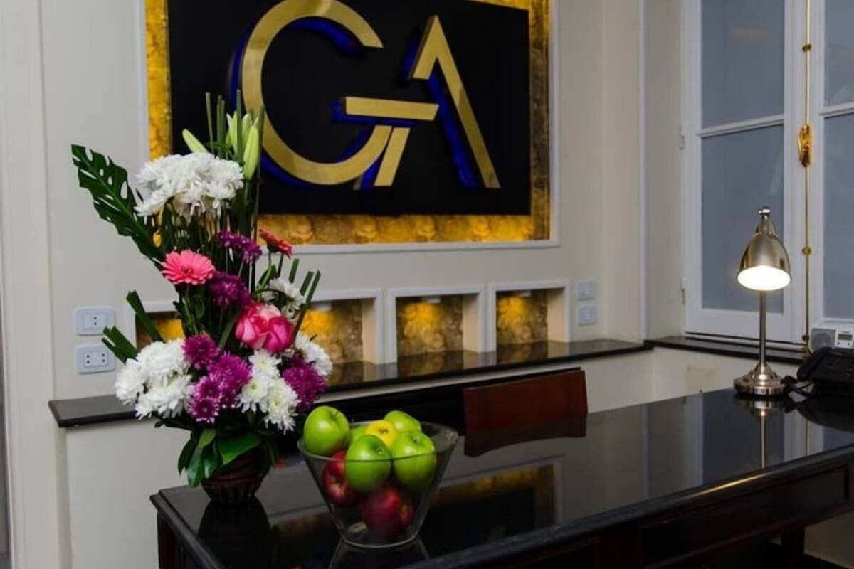 A reception desk with a vase of flowers, a bowl of apples, and a wall with a large 'GA' sign.