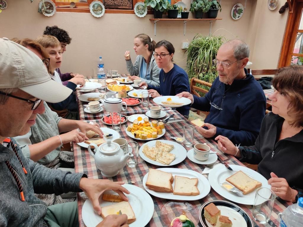 Un grupo de personas sentadas alrededor de una mesa con platos de comida, vasos y una tetera.