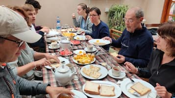 Un grupo de personas sentadas alrededor de una mesa con platos de comida, vasos y una tetera.