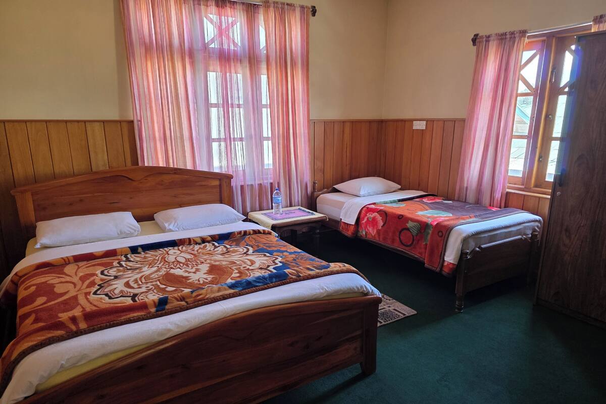 A room with two wooden beds, a small table, and a window with curtains.