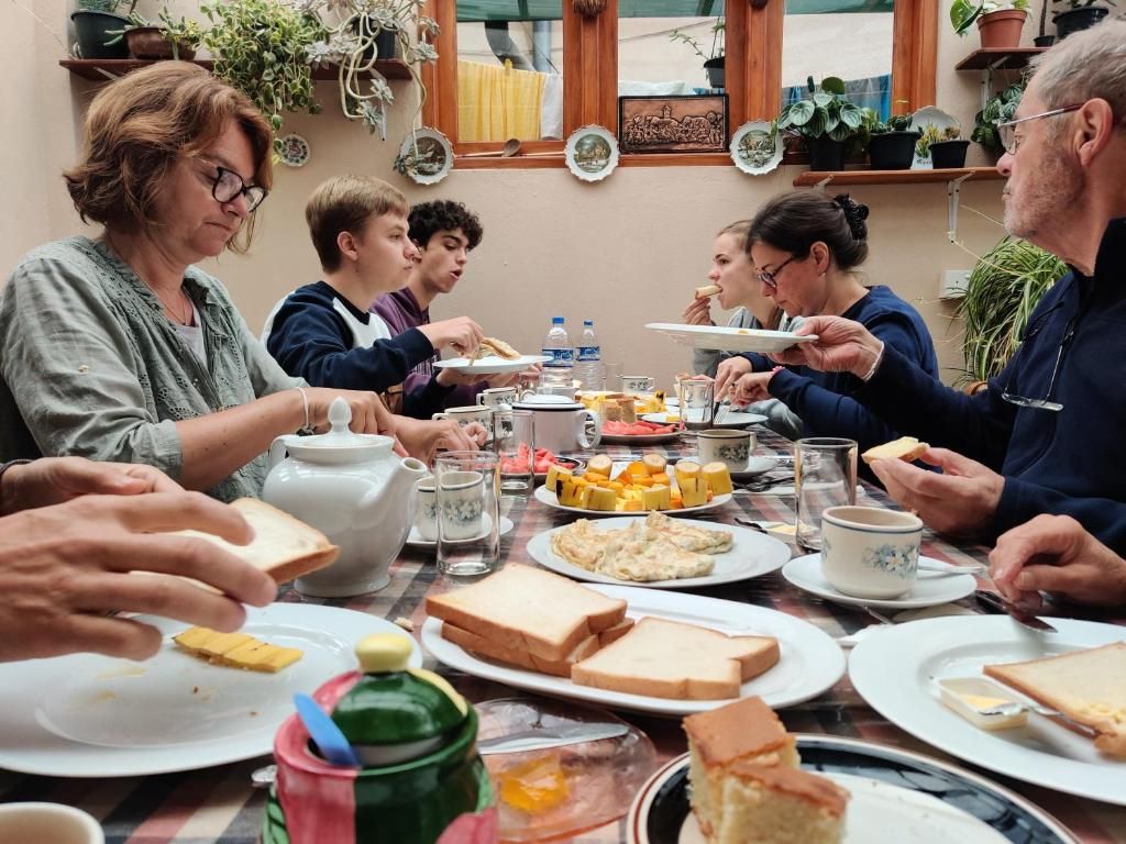A group of people dining at a table with various dishes, including bread, cheese, and a teapot.