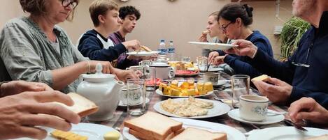 A group of people dining at a table with various dishes, including bread, cheese, and a teapot.