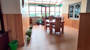 A dining area with a wooden table and chairs, potted plants, and a view through large windows. - Carnation Rest (Nuwara Eliya)