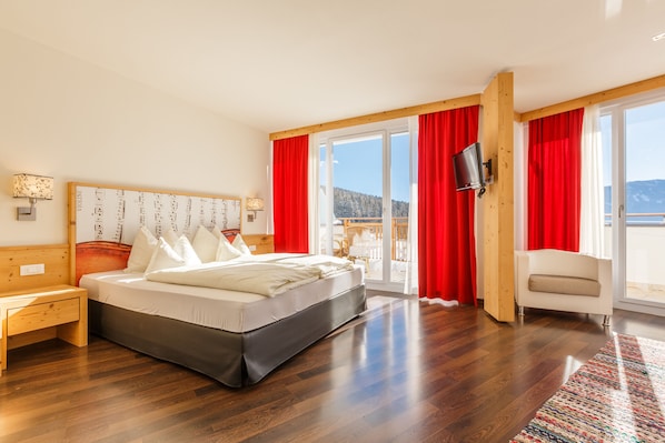 A bedroom with a bed, wooden headboard, red curtains, a TV, and a view of the outdoors. - Hotel Amaten (Brunico)
