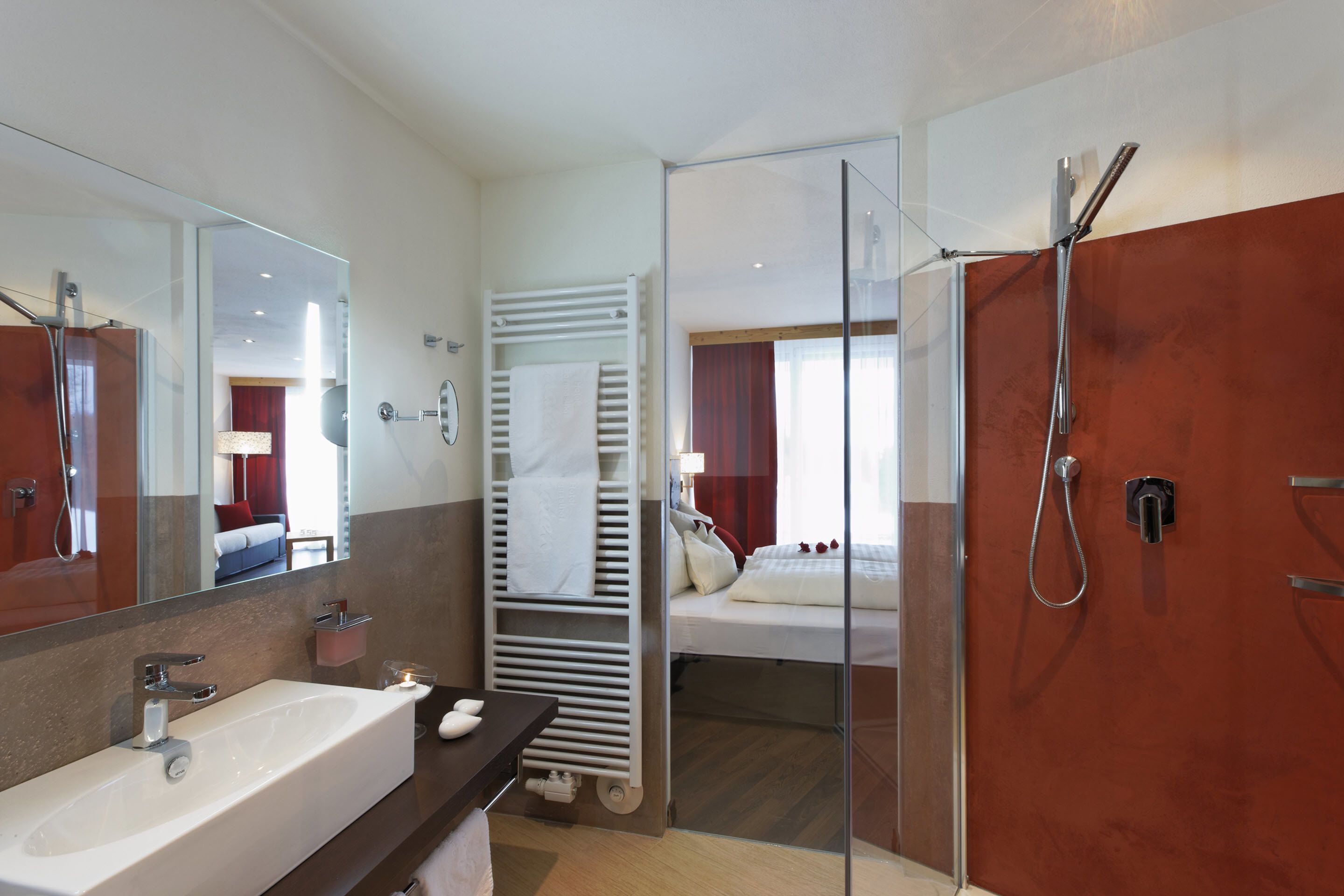 Un baño moderno con un lavamanos grande, cabina de ducha de vidrio y una cama visible en la habitación contigua.