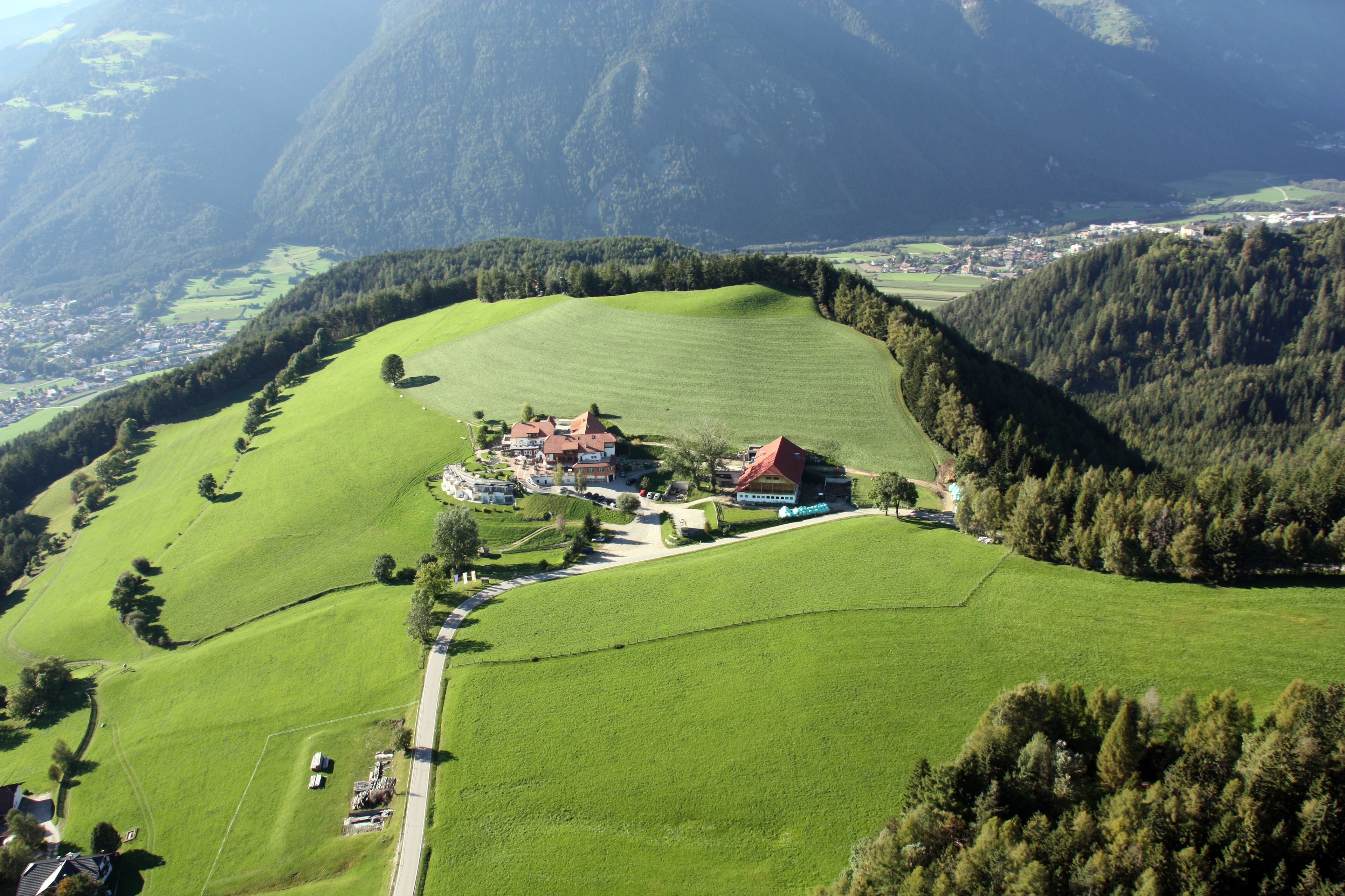 A rural landscape with a large green field, a few buildings, and a mountain in the background.