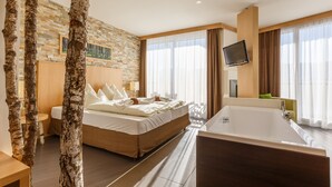Una habitación de hotel moderna con una cama grande, una bañera y una pared de piedra.
