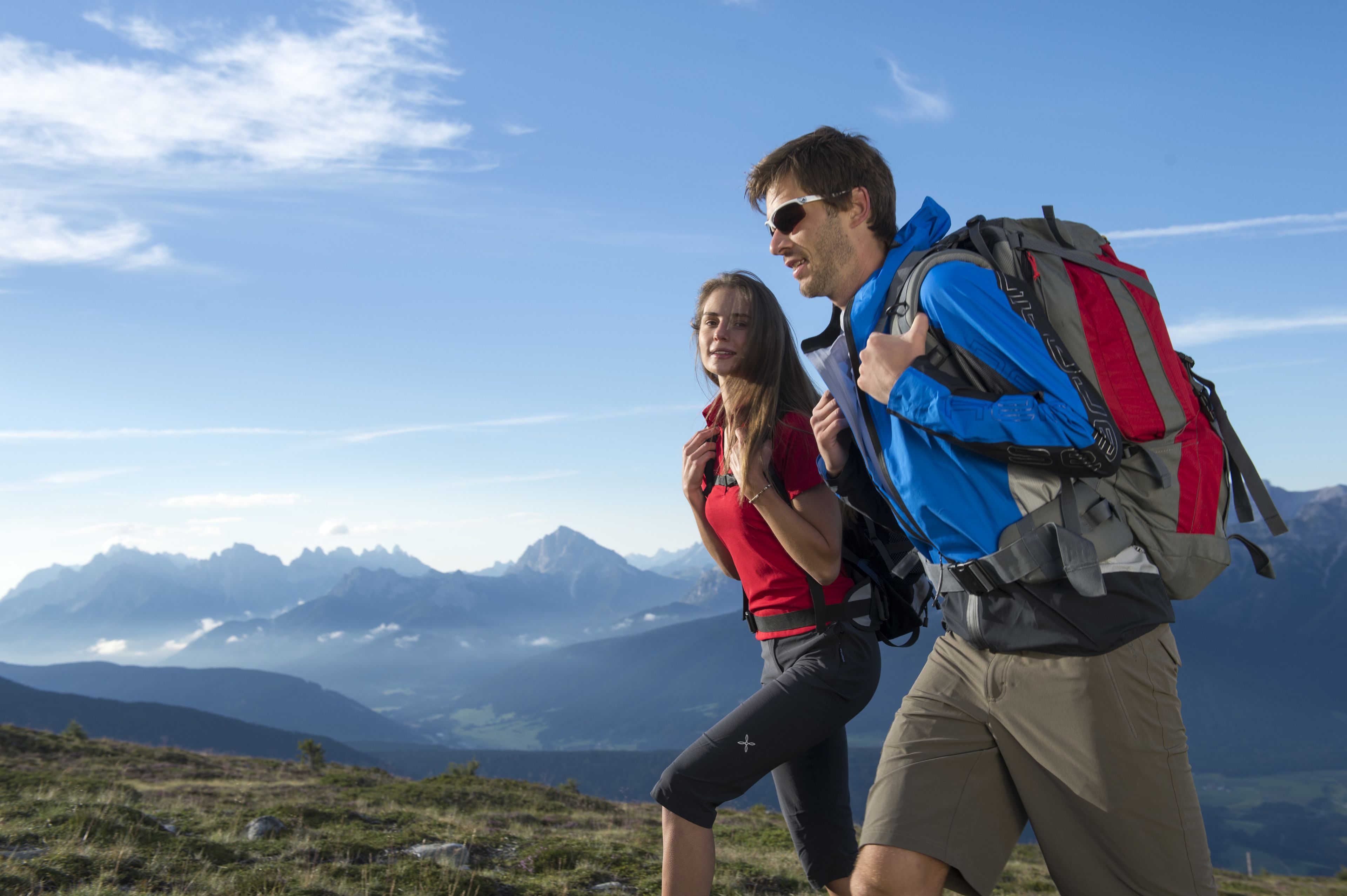 A couple hiking on a mountain trail with a clear sky and distant mountains in the background.