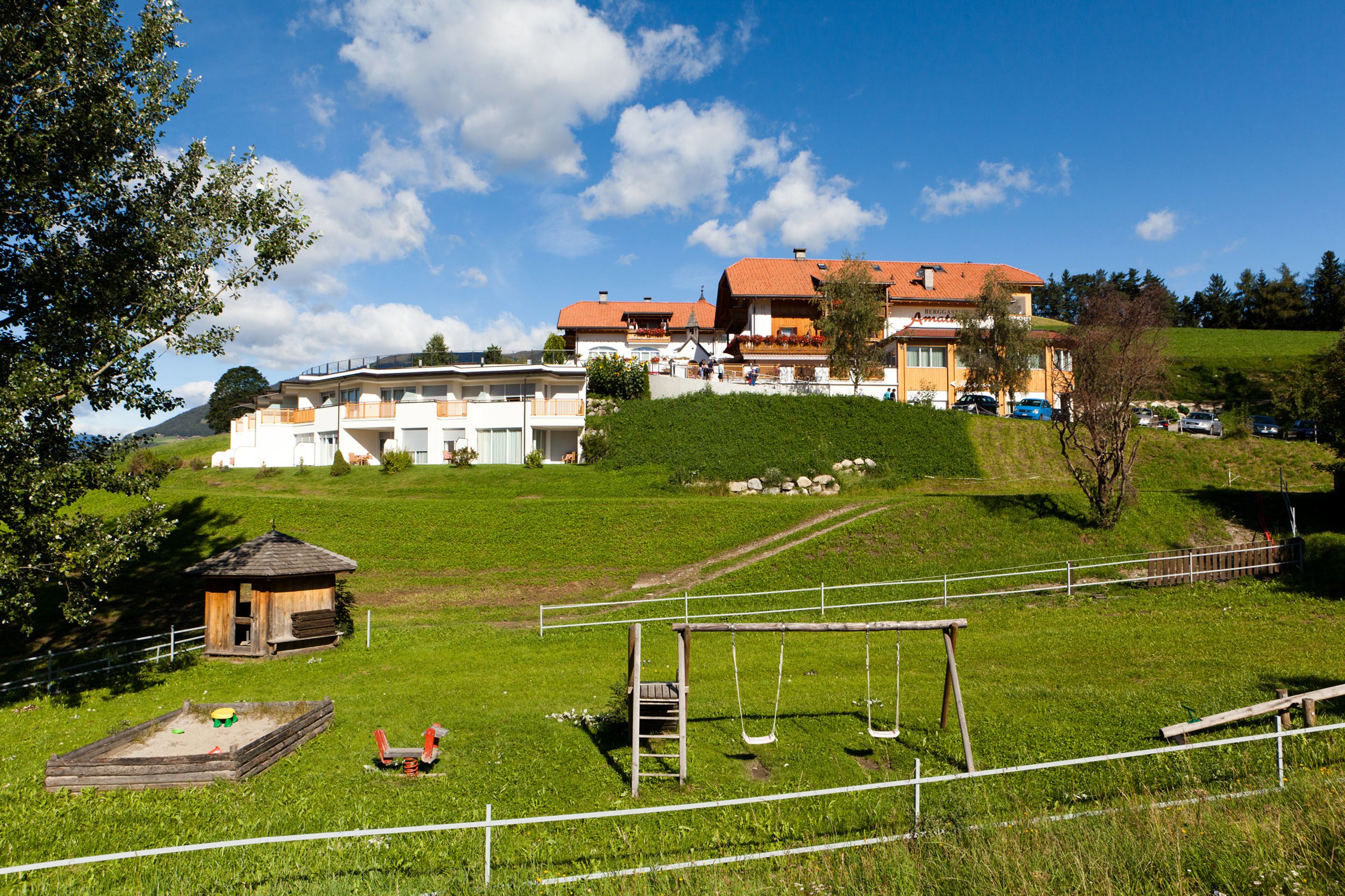 A hotel with multiple buildings, a grassy area with a swing set, and a fenced playground.