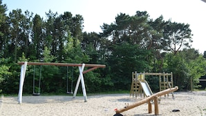 Un terrain de jeux avec des balançoires et un toboggan, entouré d’arbres.